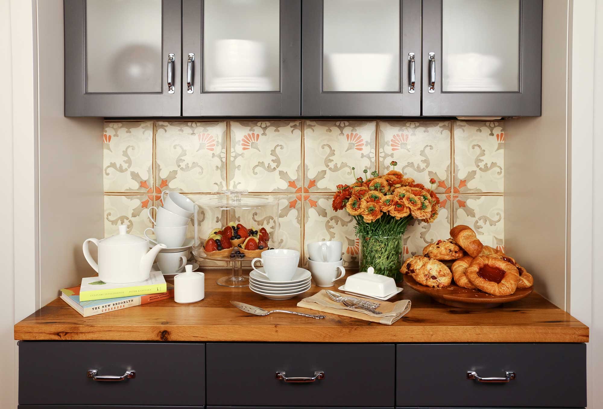 The light gray upper cabinets and dark gray base cabinets are offset with the more artistic and hand-painted custom backsplash, reclaimed antique wood countertop and red range.