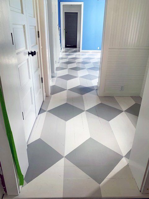 The big reveal: grey and white graphic cube illusion painted onto wood floor in series of interconnected rooms, with white and blue walls.