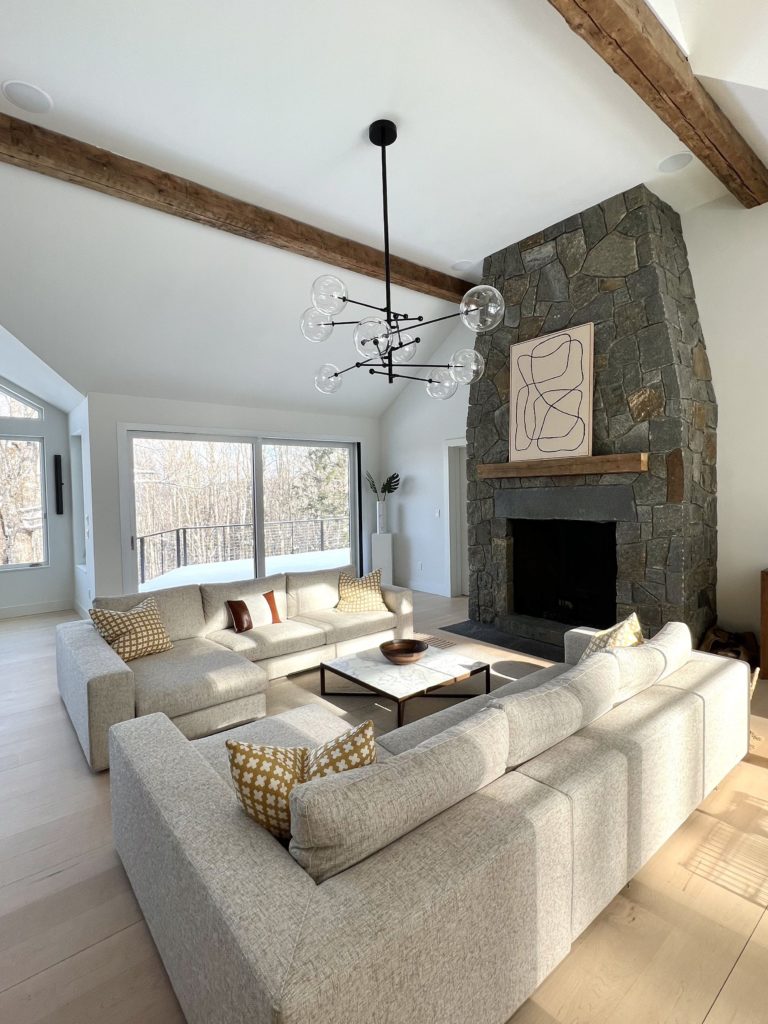 HGTV has misled you: neutral tone living room with vaulted ceiling, floor to ceiling stone fireplace, birch flooring, and view of sunny, winter day from porch.