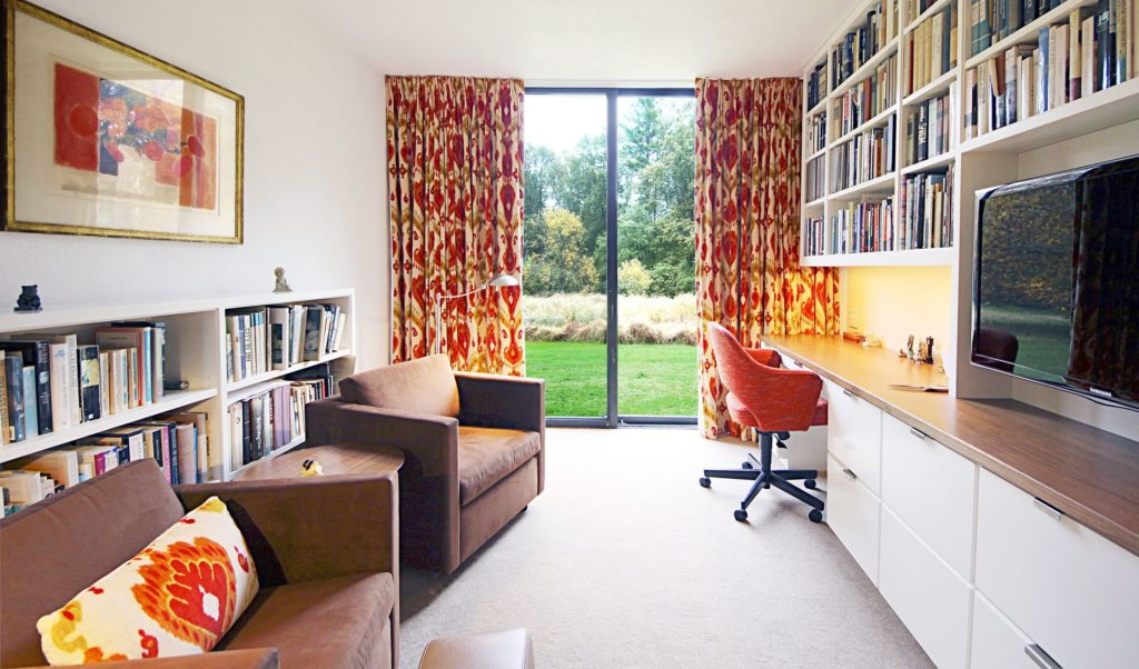 Start big and refine: home office with yellow and red curtains framing window view of grass and tress, with brown chairs, white bookshelves and desk.