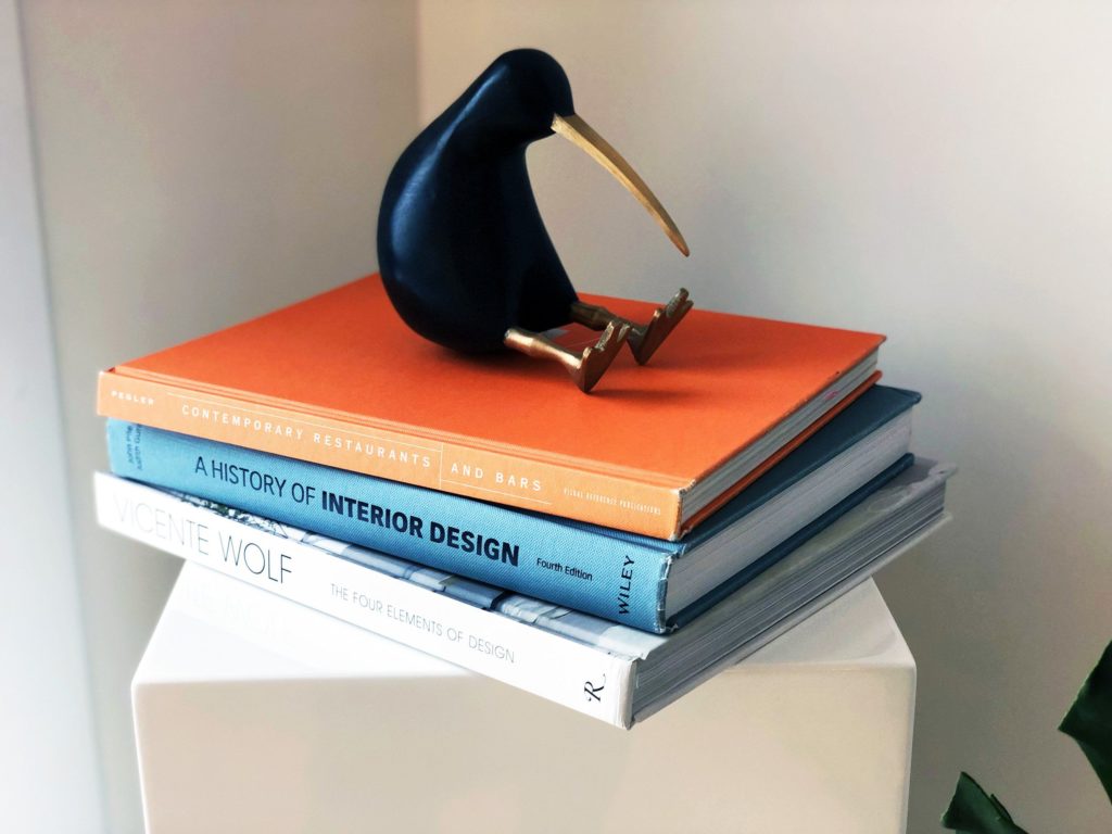 Keystone habits: a black and gold kiwi figurine sits on a stack of three design books, orange, blue and white.