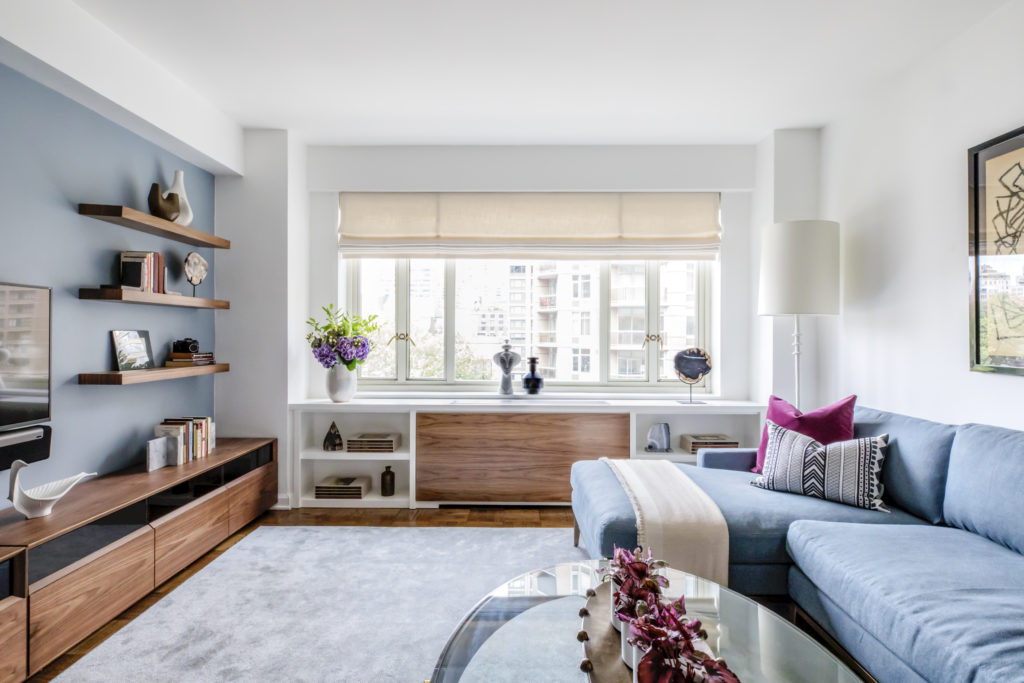 Habits that can change your life: blue, white and wood living room with oval glass coffee table in foreground, and windows looking out on the city.