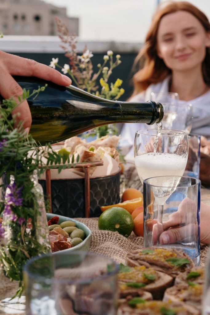 Habits that can change your life: a beautifully laid dinner table on a city rooftop has a hand pouring sparkling wine in the foreground, and a young, red haired woman in the background.