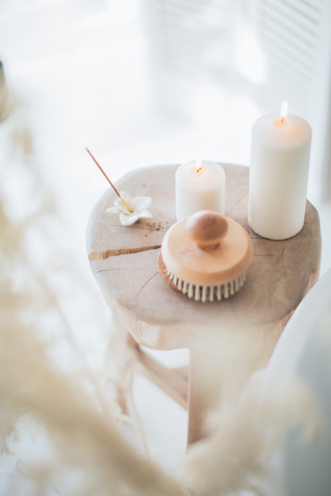 Playing the long game with luxury: natural wood stool with candles, incense and body brush, all drenched in sunlight.